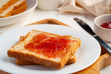 Toast bread and Strawberry Jam.Spreading jam on slice whole wheat bread in white plate.