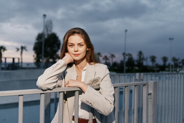 Young woman in beige blazer outdoors with confident expression during cloudy evening, urban...