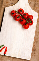 Italian tomatoes on a white wooden board with rustic brown wood background and peppers around it. Top view. Copy space.
