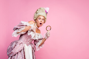 Elegant woman in historical baroque costume with corset and magnifying glass on pink background