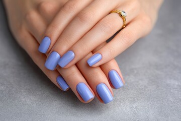 Hands with periwinkle nails  a gold ring rest on a gray surface