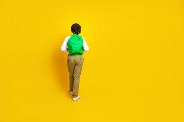 Rear view of a young boy with a backpack in vibrant clothing walking against a bright yellow...