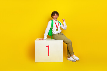 Cheerful student celebrating achievement with medal on school podium against bright yellow...