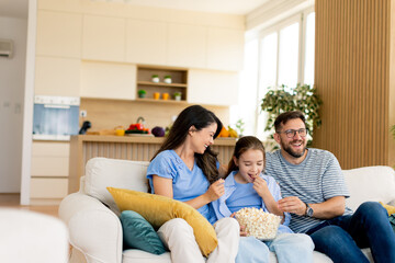 Family enjoying a cozy movie night at home with popcorn and laughter in a bright living room setting