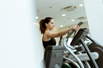 Woman exercising on an elliptical machine in a modern gym during a morning workout session focusing on fitness and health