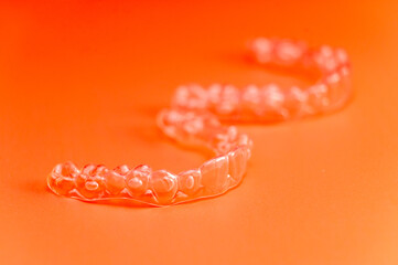 Invisible teeth retainers lie on a bright orange background. Close-up of a modern way to straighten...