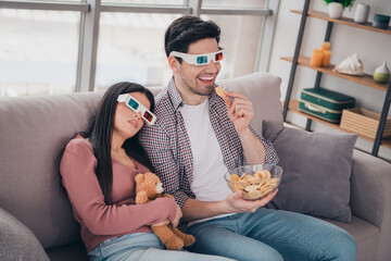 Young Couple Wearing 3D Glasses Relaxing at Home and Watching a Movie While Sharing Snacks in a Modern Living Room Setting