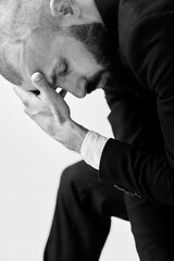 A man in a suit, head in hands, looking contemplative in a monochrome portrait.