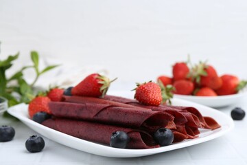 Tasty fruit leather rolls, strawberries and blueberries on white table, closeup. Space for text