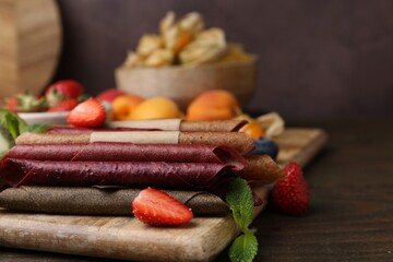 Tasty candied leather rolls, fruits and berries on wooden table, closeup