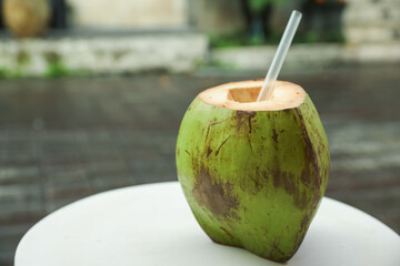 Green coconut with refreshing drink and straw on white table outdoors, closeup. Space for text