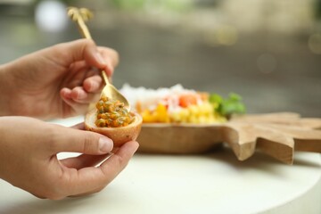 Woman eating passion fruit at table outdoors, closeup