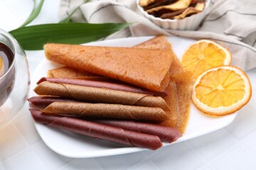 Tasty fruit leather rolls and orange slices on white table, closeup