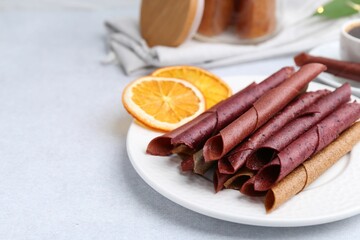 Tasty fruit leather rolls and orange slices on white table, closeup. Space for text