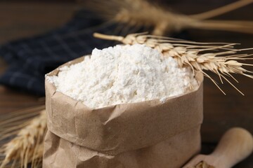 Wheat flour and spikes on wooden table, closeup