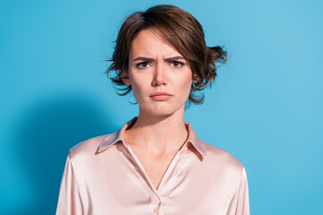 Stylish young woman in satin blouse expressing curiosity with a serious gaze against blue backdrop.
