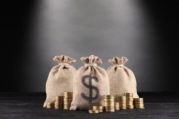 Bags with dollar sign and stacked coins on black wooden table against gray gradient background