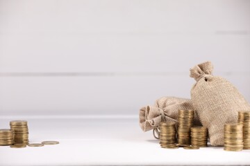 Bags and stacked coins on white table against light background, space for text