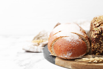 Freshly baked loaves of bread and spikes on white marble table, closeup. Space for text