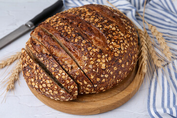 Freshly baked loaf of bread with oat flakes and spikes on light textured table, closeup