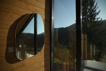 Beautiful mirror on wooden wall near window indoors