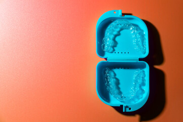 Blue plastic case with transparent brackets on a peach background. Invisible removable retainers...
