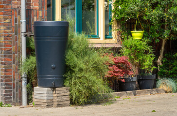 Plastic Rain Barrel Connected to Downspout on City Street, Eco-Friendly Rainwater Harvesting for Reuse
