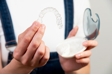 Hands of a young Caucasian woman holding transparent dental aligners and a case for storing them....