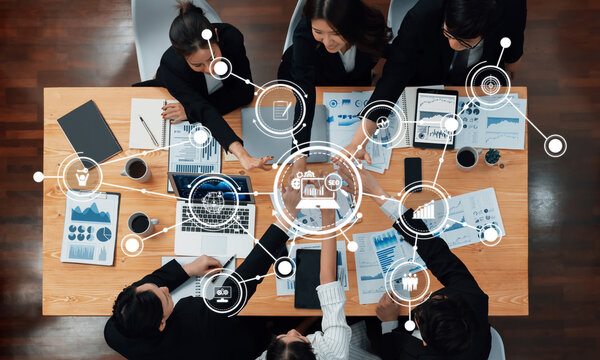 An overhead view of a collaborative business meeting showcasing professionals discussing data analysis and innovative strategies in a modern office setting. Amity