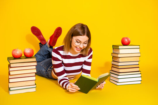 Young woman reading a book surrounded by tall stacks of book and apples on a vivid yellow background
