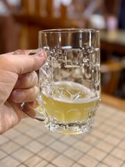 A hand joyfully holds a beer mug in a lively bar with friends and family around. A hand enthusiastically raises a frosty beer mug in a lively social setting, ideal for celebrating joyful moments