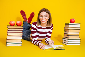 Smiling young woman lying on floor surrounded by book and apples, enjoying a casual day of reading...