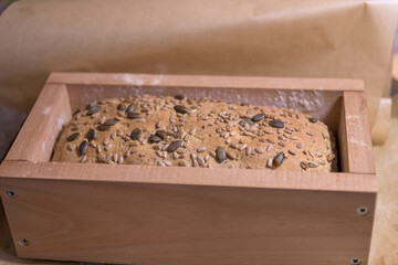 Homemade seed bread dough resting in a wooden mold with grains before baking in a rustic kitchen