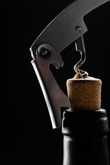 
Wine bottle being opened with corkscrew on table on black background.