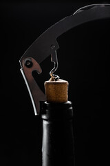 
Wine bottle being opened with corkscrew on table on black background.