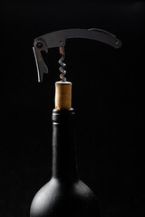 
Wine bottle being opened with corkscrew on table on black background.