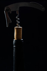 
Wine bottle being opened with corkscrew on table on black background.
