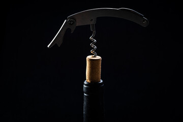 
Wine bottle being opened with corkscrew on table on black background.