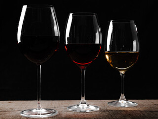 Crystal glasses with red and white wine
over rustic wooden table on black background