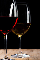 Crystal glasses with red and white wine
over rustic wooden table on black background