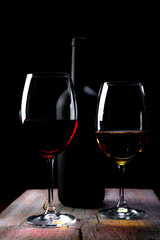 Crystal glasses with red and white wine and wine bottles,
over rustic wooden table on black...