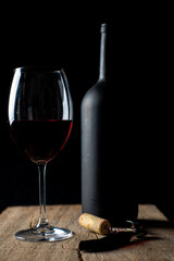 
Glass of red wine on the rustic wooden table, with corkscrew beside it and defocused wine bottle on black background.