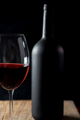 Crystal goblet with red wine and bottle on the rustic wooden table on black background