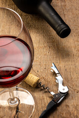 
Glass of red wine on the rustic wooden table, with corkscrew beside it and defocused wine bottle...