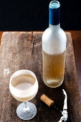 Crystal glass with white wine and bottle of wine served very cold,
over rustic wooden table on...