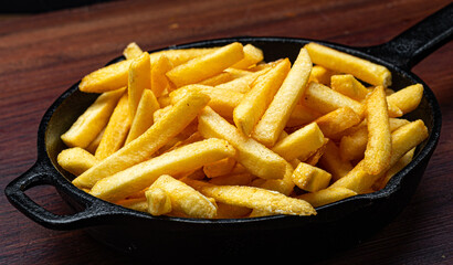 Portion of french fries served in an iron pan on a wooden background, top view