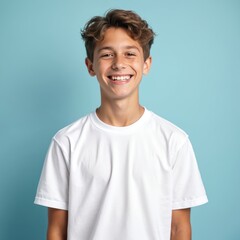 Happy caucasian teenage boy in white t-shirt smiling on blue background. Portrait of cheerful young male, person with positive emotions. Kid with dark hair and photogenic face. T-shirt mockup.
