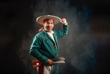 A man in a green shirt and hat is holding two knives