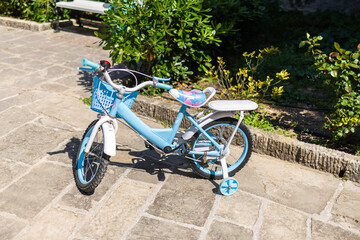 Blue kids bicycle with training wheels on sunny pavement. Childhood fun, outdoor learning, and the...