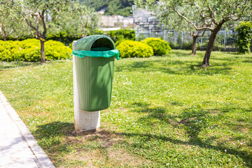 Green park trash bin in spring sunlight. Clean environment, urban maintenance, and public...
